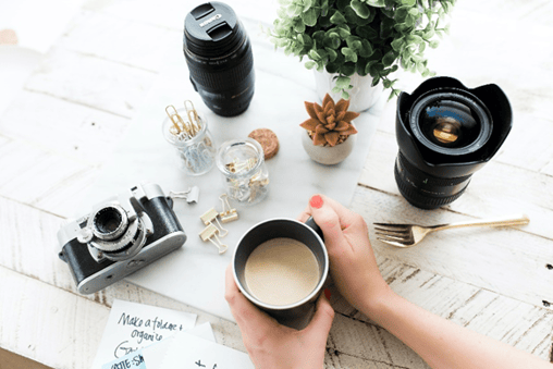 A cup of coffee surrounded by cameras and camera lenses.