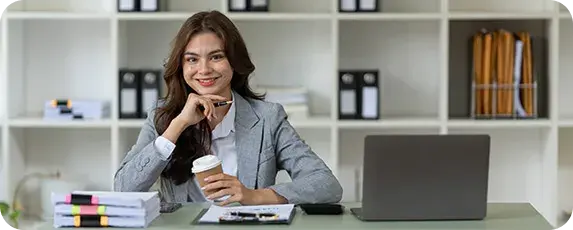 Professional woman in a modern office setting using a laptop, holding a coffee cup and smiling—representing streamlined ecommerce accounting with Xero automation.