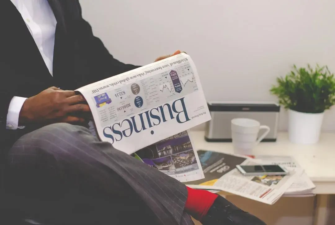 A businessman in a suit reads an upside-down business newspaper in an office, with a coffee cup, smartphone, and financial papers nearby—symbolizing CFO performance metrics and eCommerce financial health.